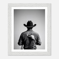 Black and white photograph of a rodeo cowboy viewed from behind wearing a western hat with a numbered rodeo tag pinned to his shirt after competition.
