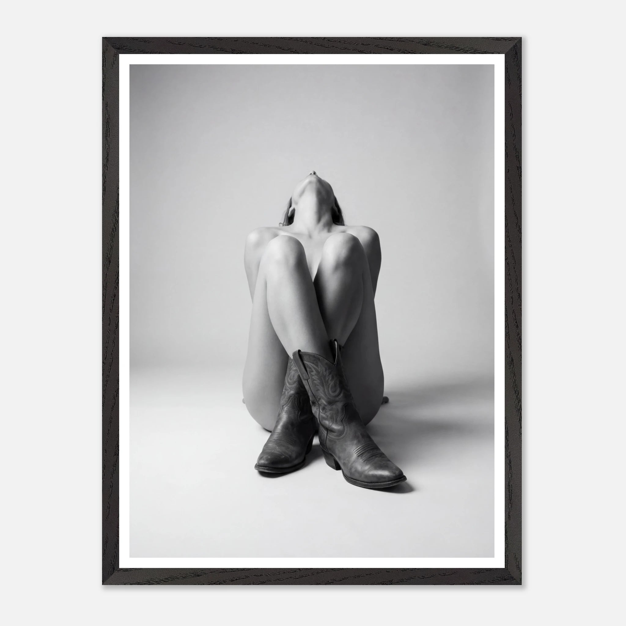 Framed black and white art print of a person wearing cowboy boots sitting on the floor.