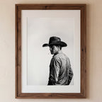 Black and white photograph of a rodeo cowboy wearing a western hat and cigarette, turning toward the camera after competition, western cowboy wall art poster.