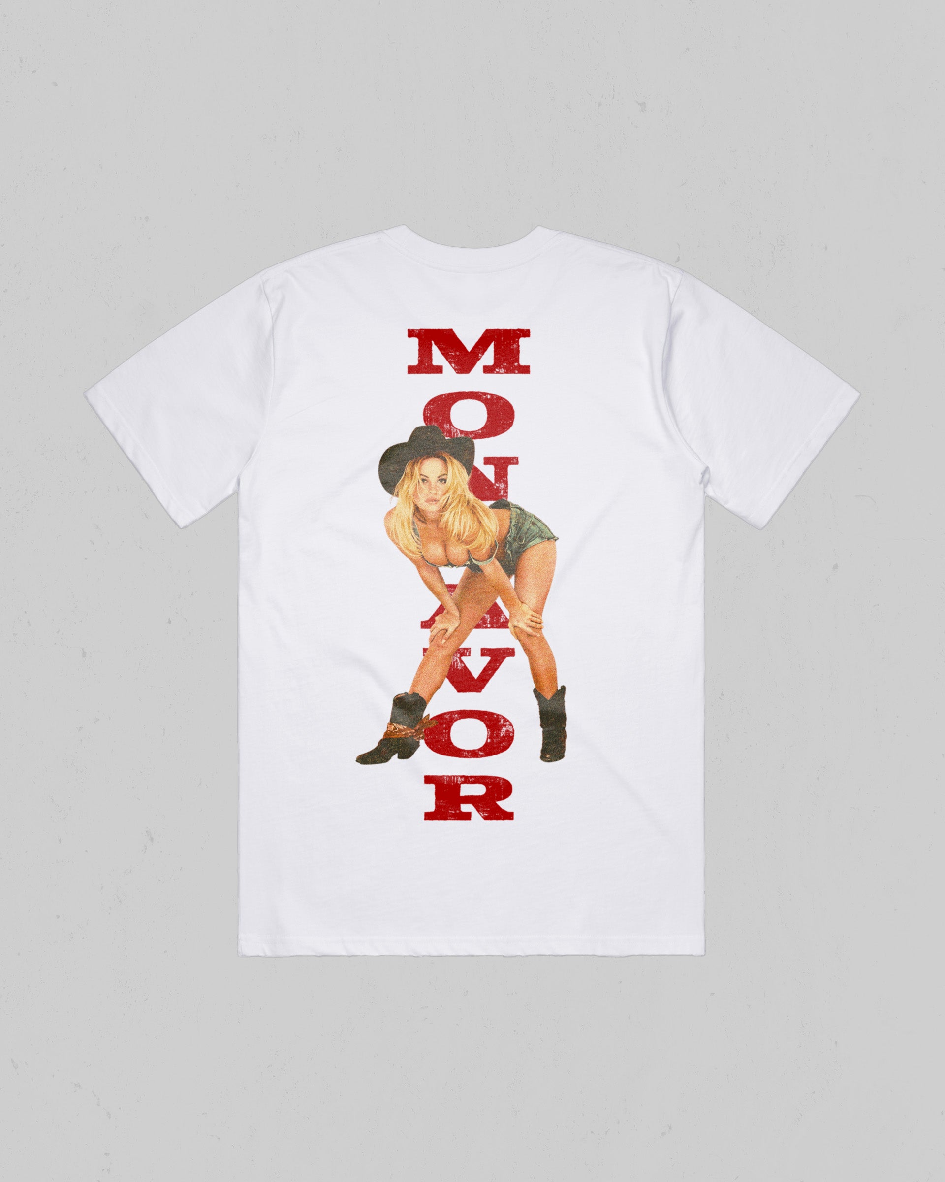 A white short-sleeve t-shirt laid flat against a light gray background, featuring a large graphic print on the back with the words 'MONTAVOR' in distressed red letters and an illustration of a blonde woman in a cowboy hat and boots.