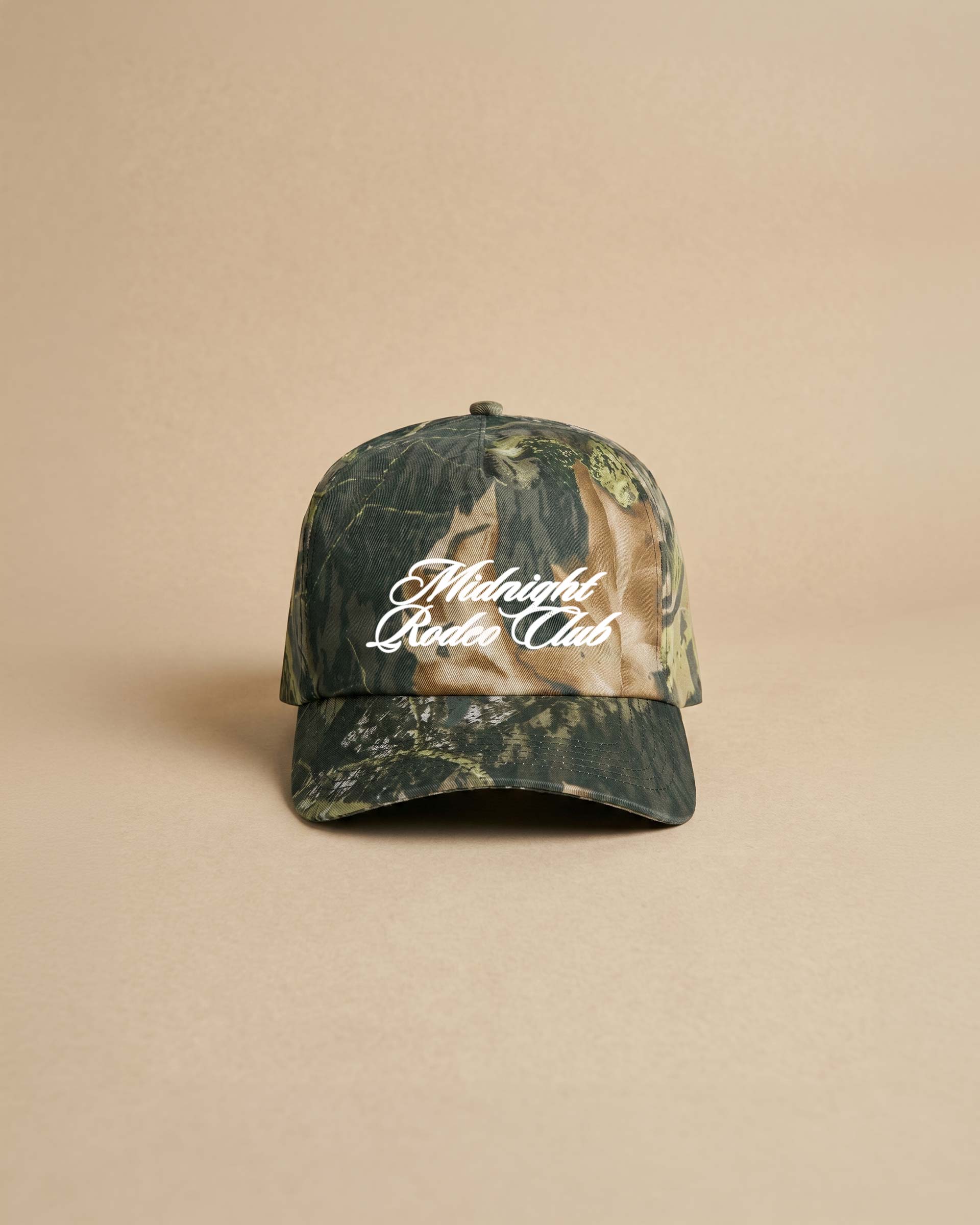 Camouflage baseball cap with 'Midnight Rodeo Club' text on a beige background