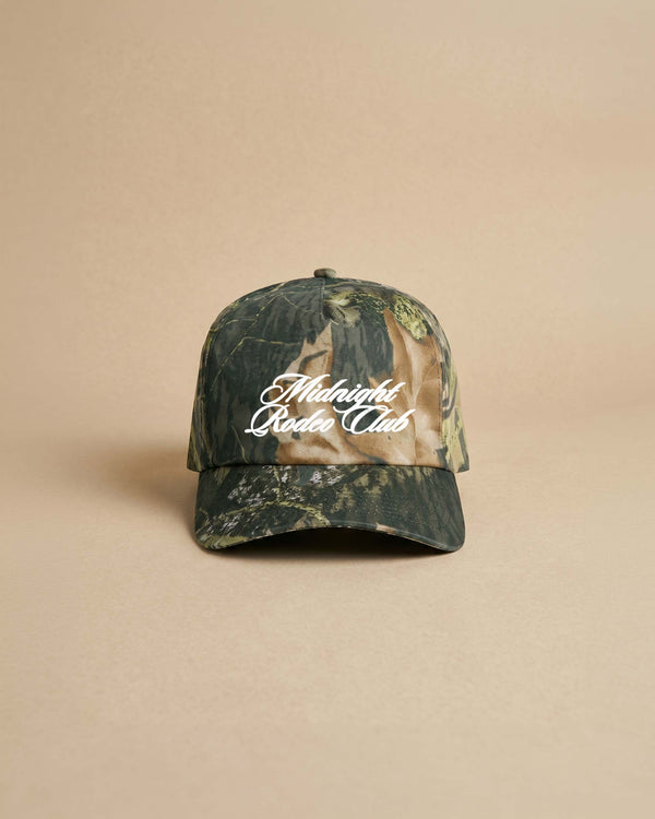 Camouflage baseball cap with 'Midnight Rodeo Club' text on a beige background