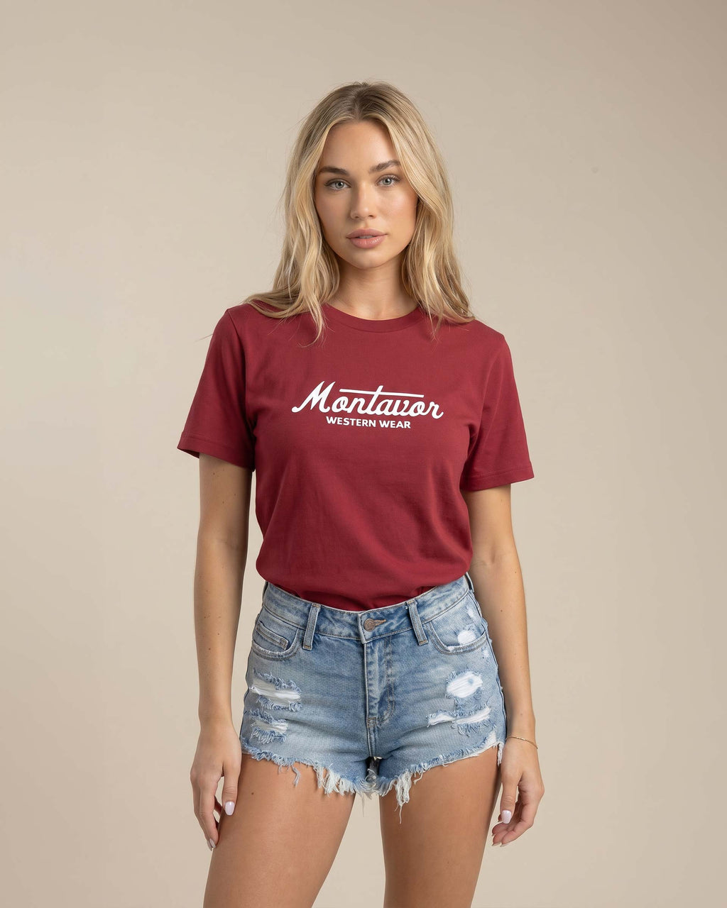 Woman wearing a maroon t-shirt with 'Montavor' logo and denim shorts on a beige background