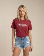 Woman wearing a maroon t-shirt with 'Montavor' logo and denim shorts on a beige background