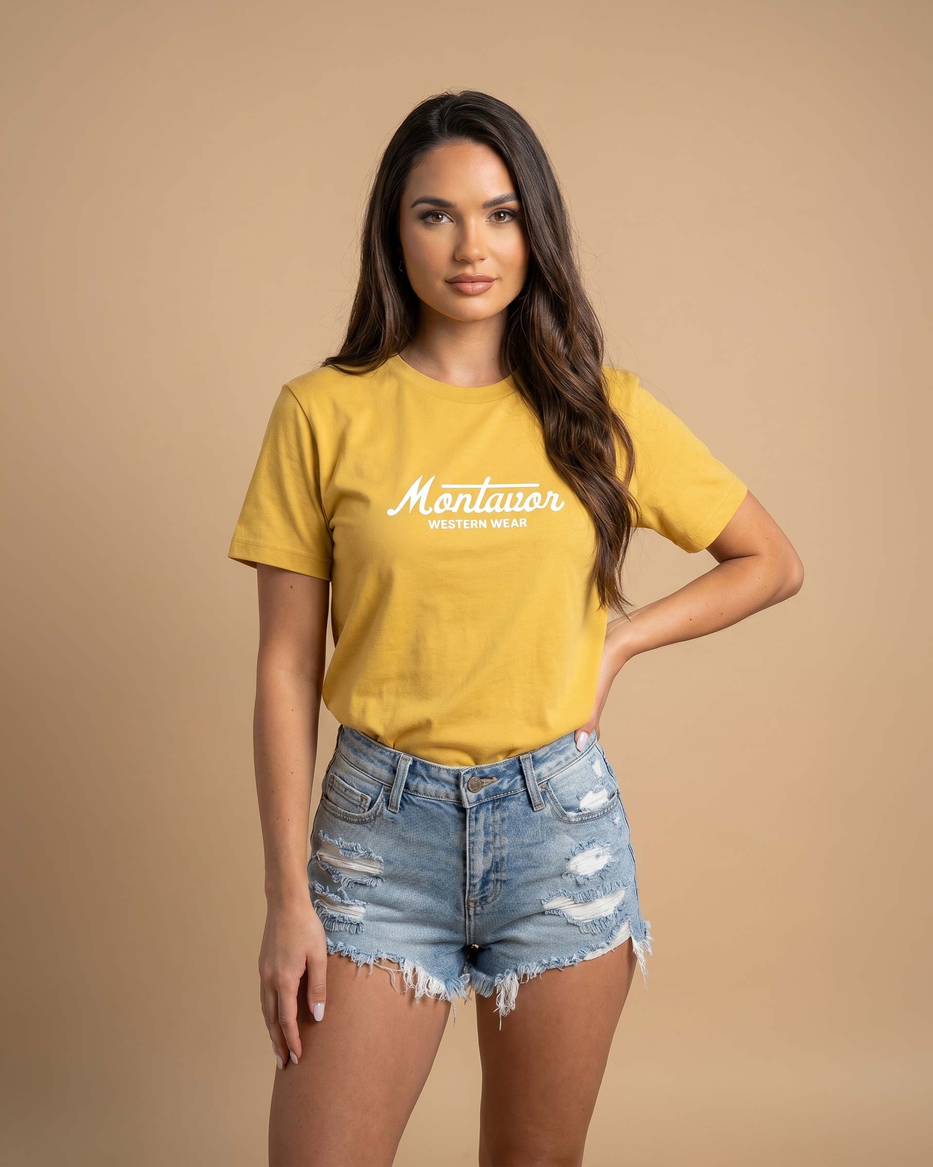 Woman wearing a yellow t-shirt with text and denim shorts on a beige background