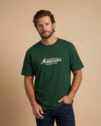 Man wearing a green t-shirt with 'Montavor Western Wear' logo against a beige background