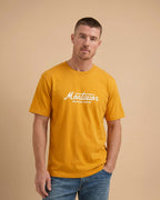 Man wearing a mustard yellow t-shirt with 'Montavor Western Wear' logo on a beige background