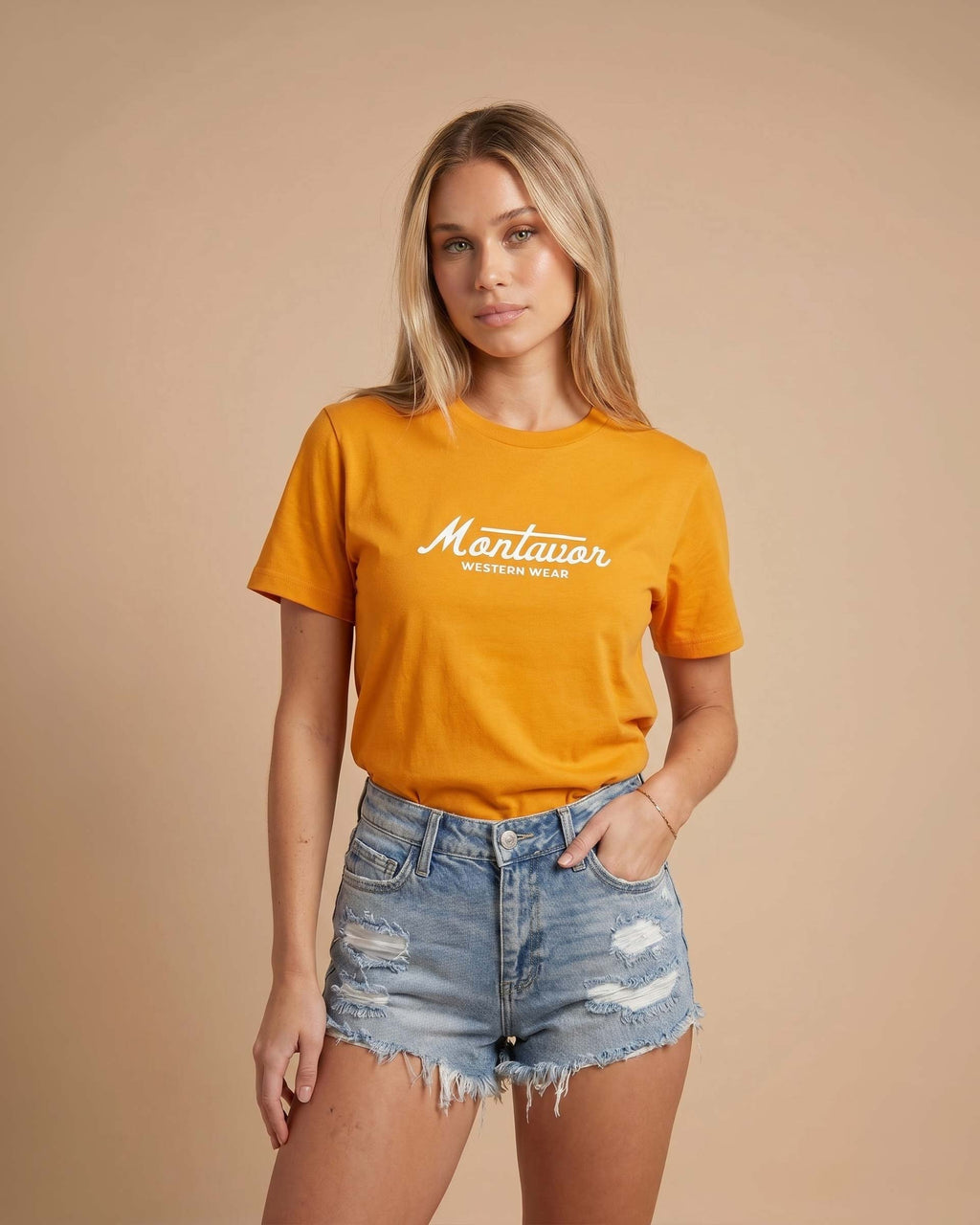 Woman wearing an orange t-shirt with 'Montavor' text and denim shorts on a beige background