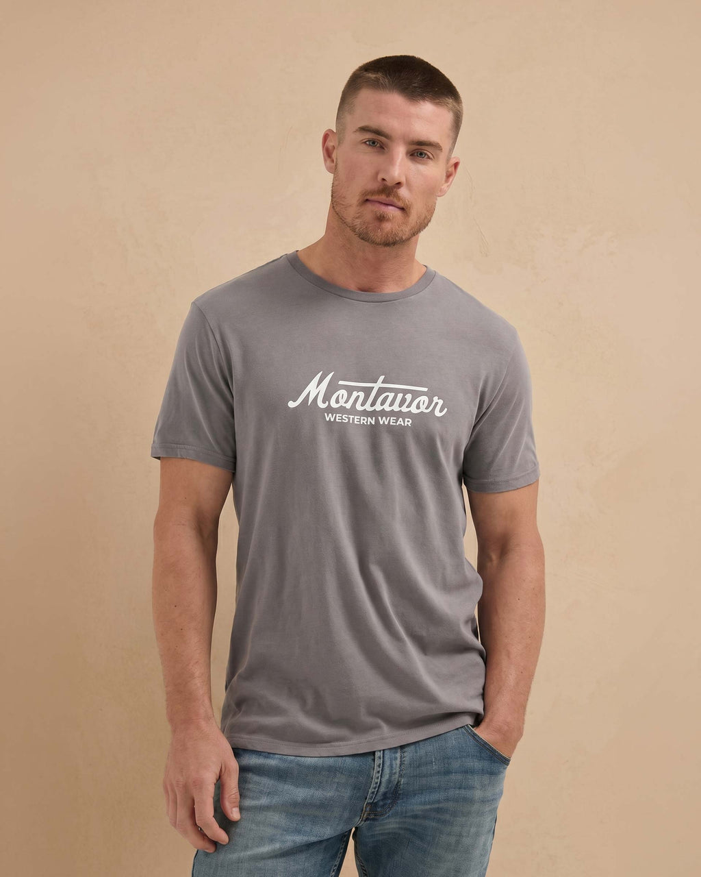 Man wearing a gray t-shirt with 'Montavor Western Wear' logo on a beige background