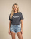 Woman wearing a dark gray t-shirt with 'Montavor Western Wear' text and denim shorts on a beige background