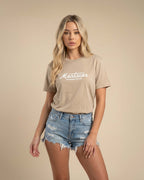 Woman wearing a beige t-shirt with 'Montavor' text and denim shorts on a beige background
