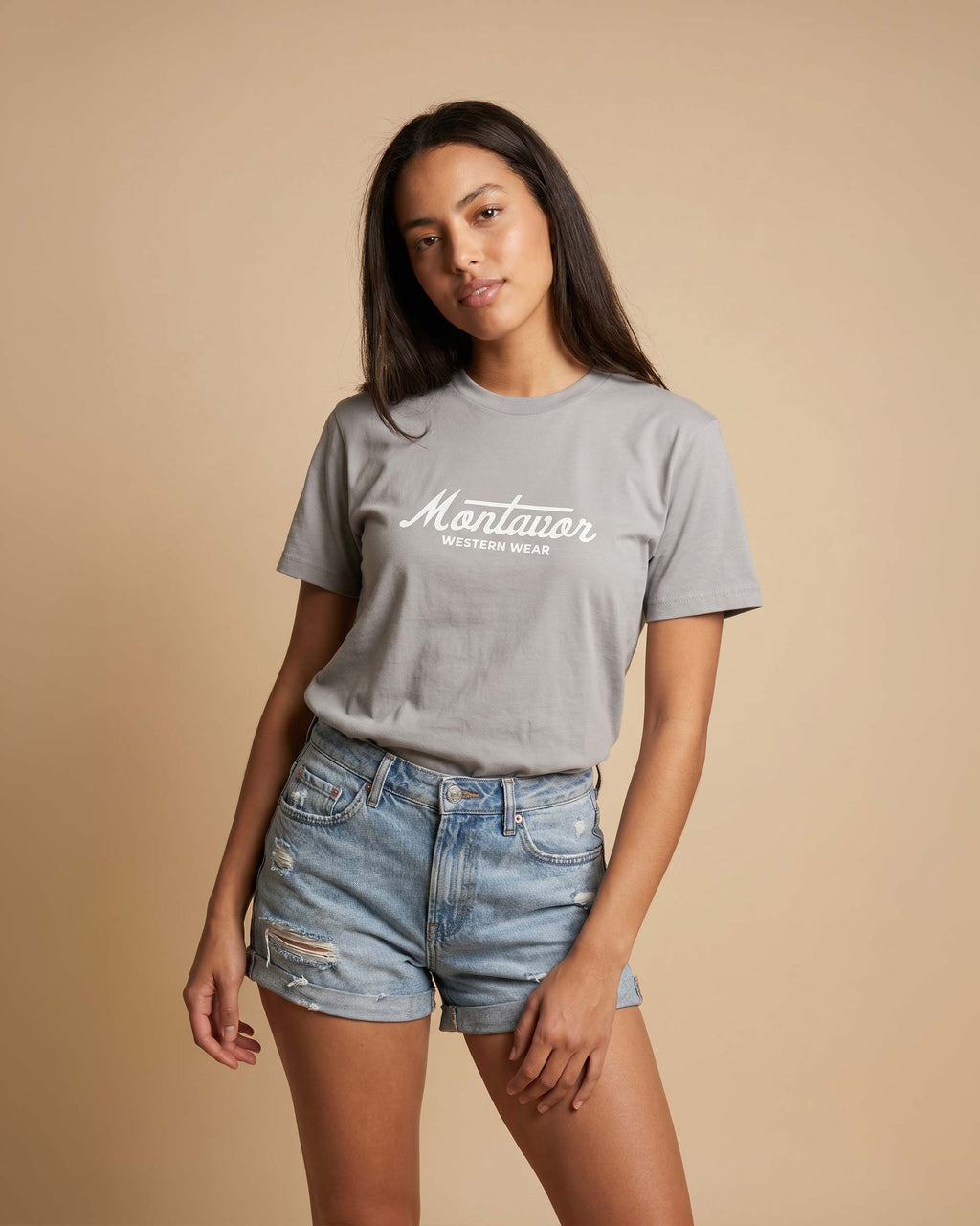 Woman wearing a gray t-shirt with 'Montavor' text and denim shorts on a beige background