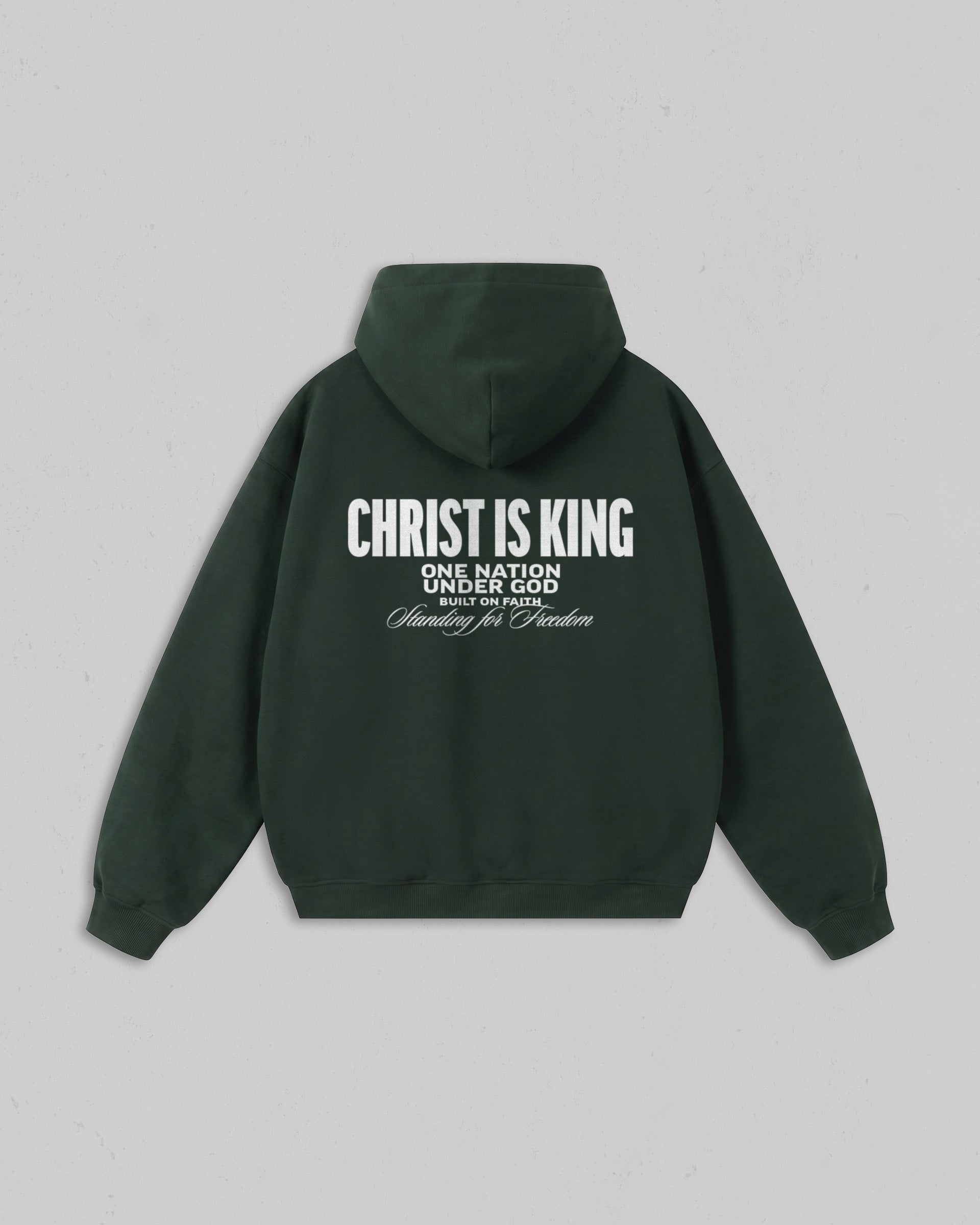 A dark forest green hoodie shown from the back, featuring white printed text that reads 'CHRIST IS KING' with smaller text below reading 'ONE NATION UNDER GOD' and 'Standing for Freedom'. The hoodie is displayed flat against a neutral light gray background. Main image