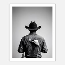 Black and white photograph of a rodeo cowboy viewed from behind wearing a western hat with a numbered rodeo tag pinned to his shirt after competition.