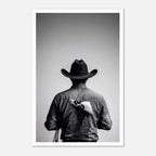 Black and white photograph of a rodeo cowboy viewed from behind wearing a western hat with a numbered rodeo tag pinned to his shirt after competition.
