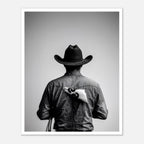 Black and white photograph of a rodeo cowboy viewed from behind wearing a western hat with a numbered rodeo tag pinned to his shirt after competition.