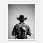 Black and white photograph of a rodeo cowboy viewed from behind wearing a western hat with a numbered rodeo tag pinned to his shirt after competition.