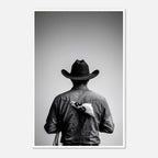 Black and white photograph of a rodeo cowboy viewed from behind wearing a western hat with a numbered rodeo tag pinned to his shirt after competition.