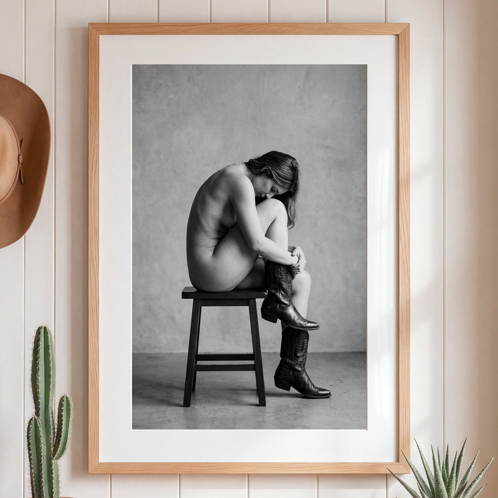 Black and white fine art photograph of a woman seated on a stool wearing cowboy boots in a minimalist studio setting. Main image