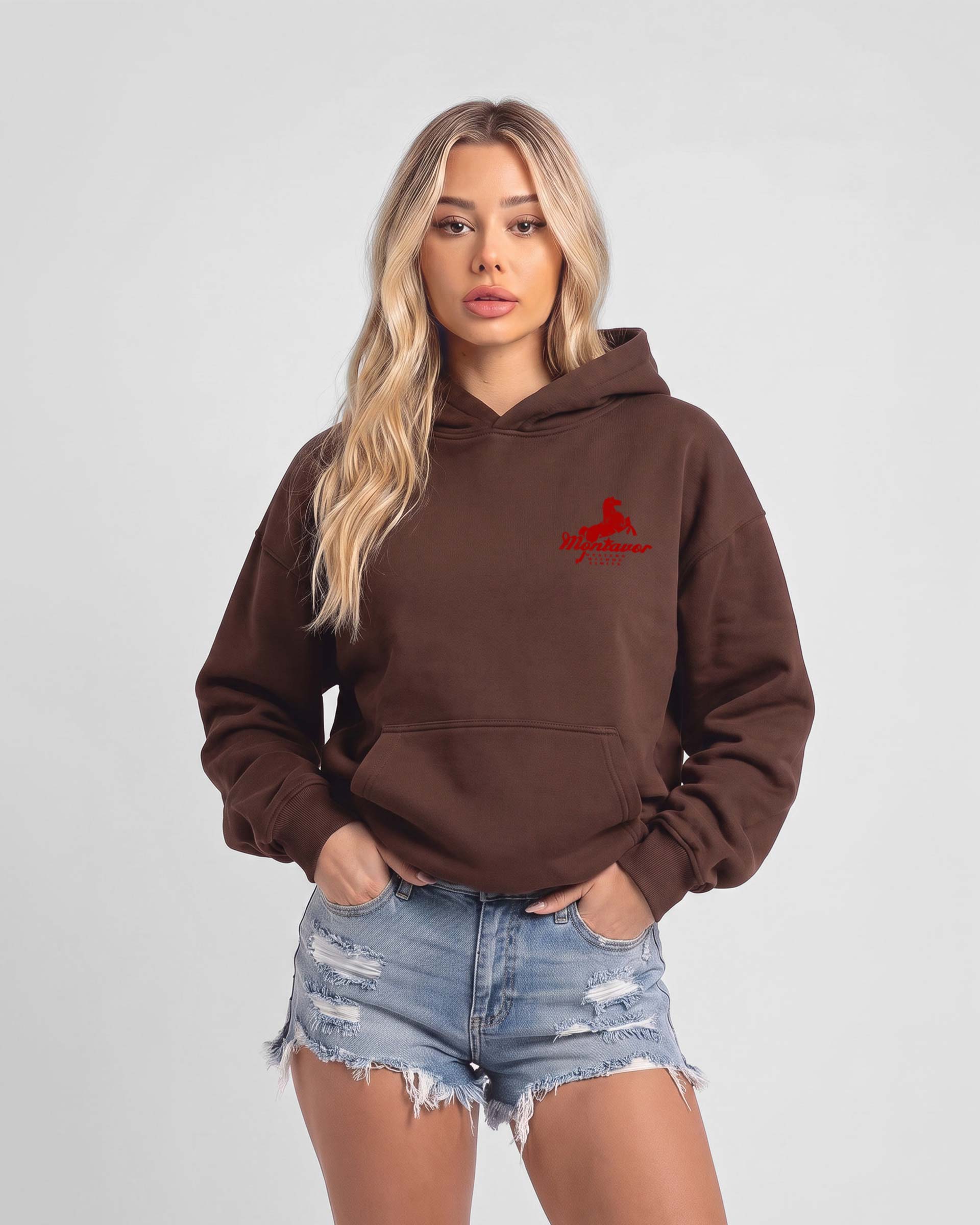 A woman shown wearing a brown pullover hoodie with'MONTAVOR' in red, paired with light blue denim shorts against a light gray studio background.
