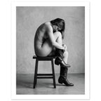 Black and white fine art photograph of a woman seated on a stool wearing cowboy boots in a minimalist studio setting.