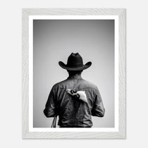 Black and white photograph of a rodeo cowboy viewed from behind wearing a western hat with a numbered rodeo tag pinned to his shirt after competition.