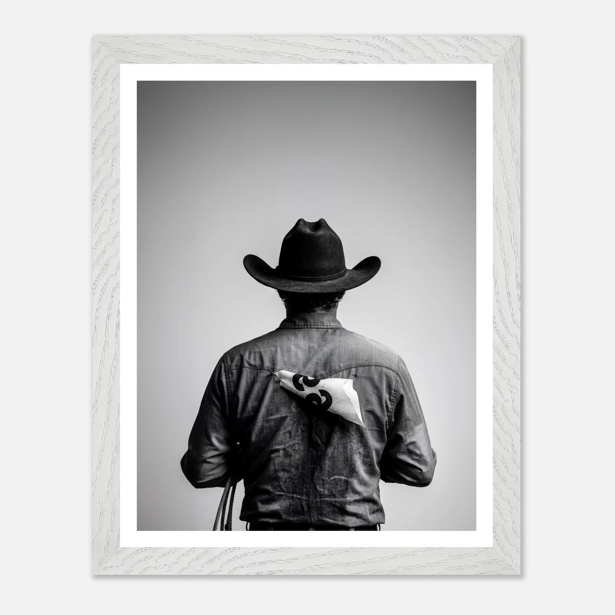 Black and white photograph of a rodeo cowboy viewed from behind wearing a western hat with a numbered rodeo tag pinned to his shirt after competition.