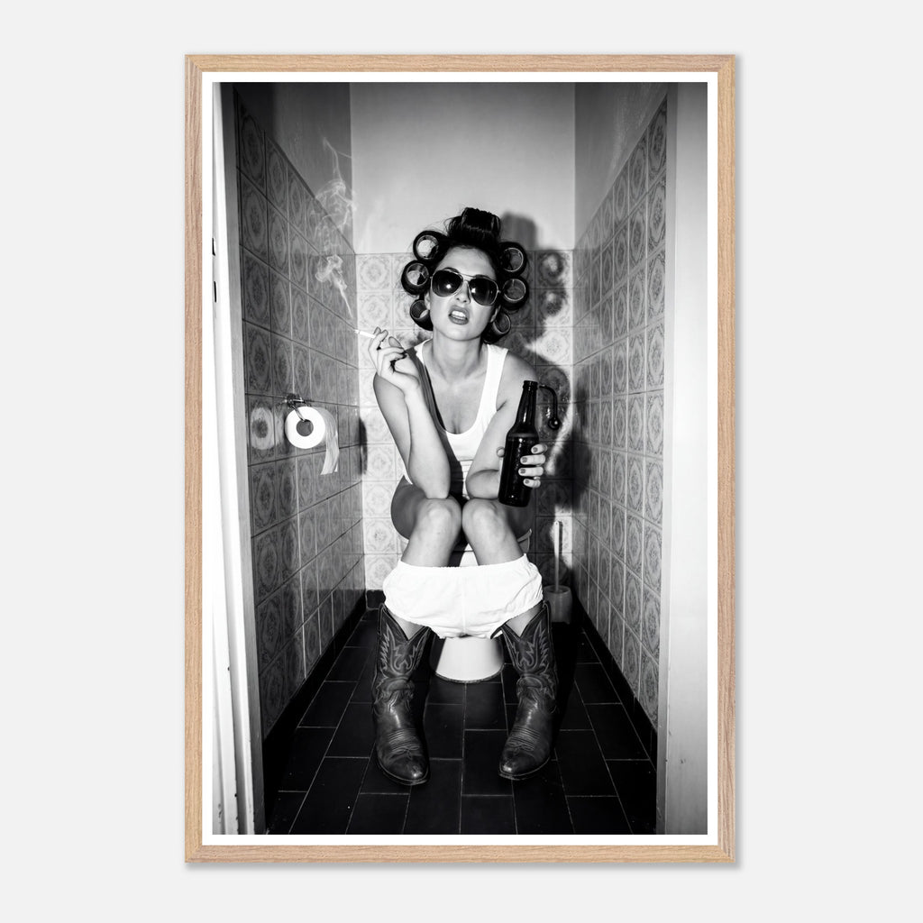 Black and white photograph of a rebellious cowgirl wearing cowboy boots and sunglasses sitting in a tiled restroom holding a cigarette and beer.