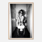Black and white photograph of a rebellious cowgirl wearing cowboy boots and sunglasses sitting in a tiled restroom holding a cigarette and beer.