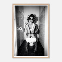 Black and white photograph of a rebellious cowgirl wearing cowboy boots and sunglasses sitting in a tiled restroom holding a cigarette and beer.