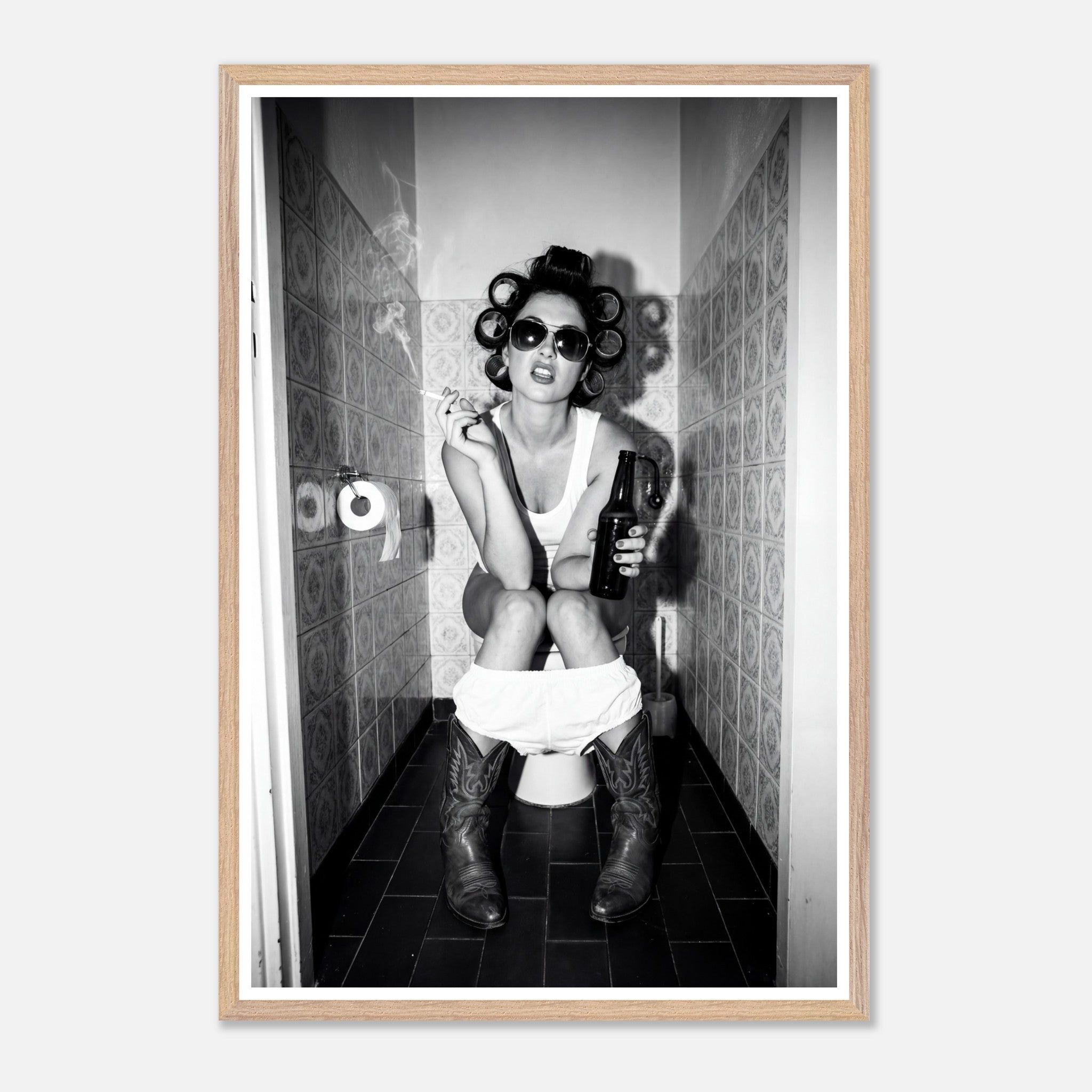 Black and white photograph of a rebellious cowgirl wearing cowboy boots and sunglasses sitting in a tiled restroom holding a cigarette and beer.