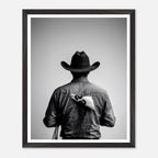 Black and white photograph of a rodeo cowboy viewed from behind wearing a western hat with a numbered rodeo tag pinned to his shirt after competition.