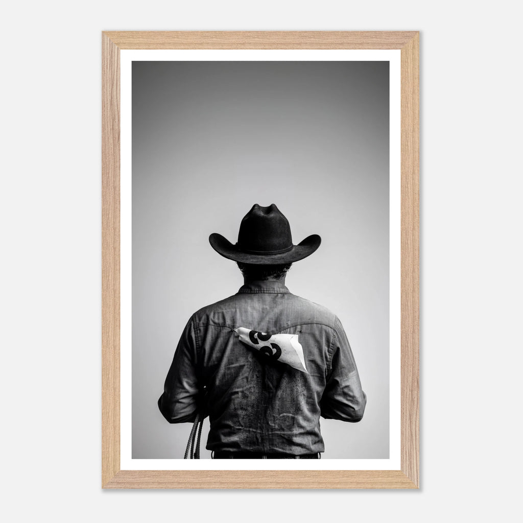 Black and white photograph of a rodeo cowboy viewed from behind wearing a western hat with a numbered rodeo tag pinned to his shirt after competition.