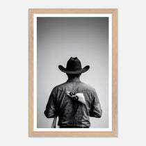 Black and white photograph of a rodeo cowboy viewed from behind wearing a western hat with a numbered rodeo tag pinned to his shirt after competition.