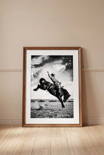 Framed black and white photograph of a cowboy riding a bucking bronco on a wall.