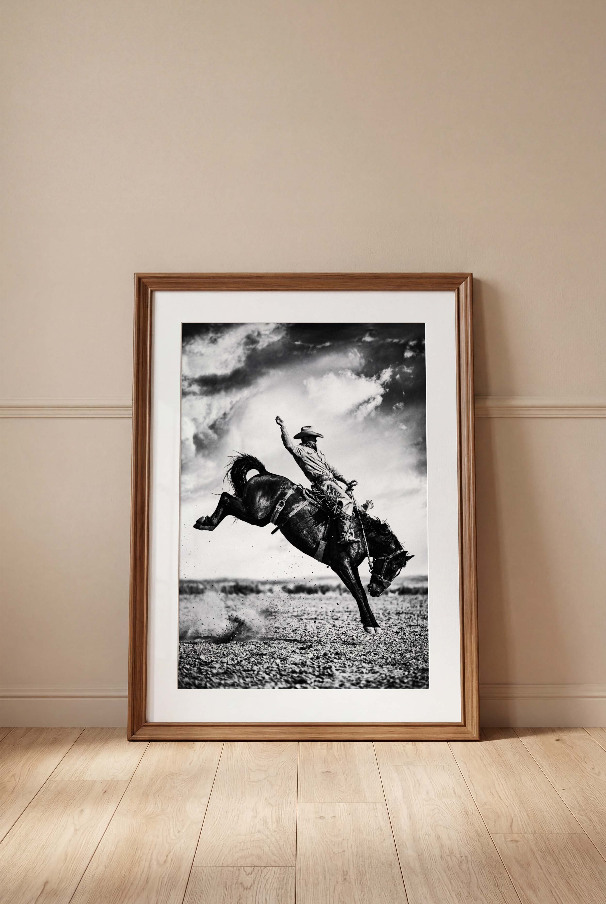 Framed black and white photograph of a cowboy riding a bucking bronco on a wall.