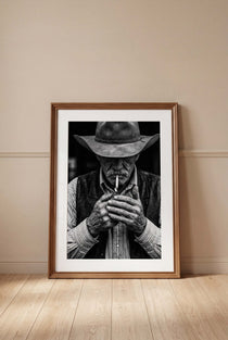 Black and white portrait of a cowboy lighting a cigarette wearing a hat, western wall art.