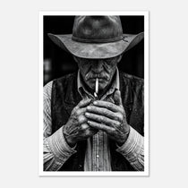 Black and white portrait of a cowboy lighting a cigarette wearing a hat, western wall art.