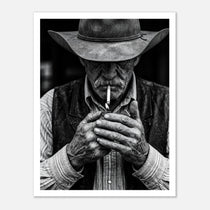 Black and white portrait of a cowboy lighting a cigarette wearing a hat, western wall art.