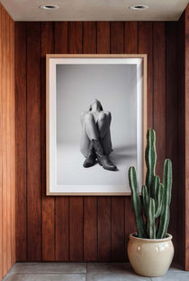 Black and white fine art poster of a seated cowgirl figure wearing classic cowboy boots against a minimalist studio background, creating a dramatic western-inspired composition.