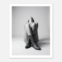 Black and white fine art poster of a seated cowgirl figure wearing classic cowboy boots against a minimalist studio background, creating a dramatic western-inspired composition.