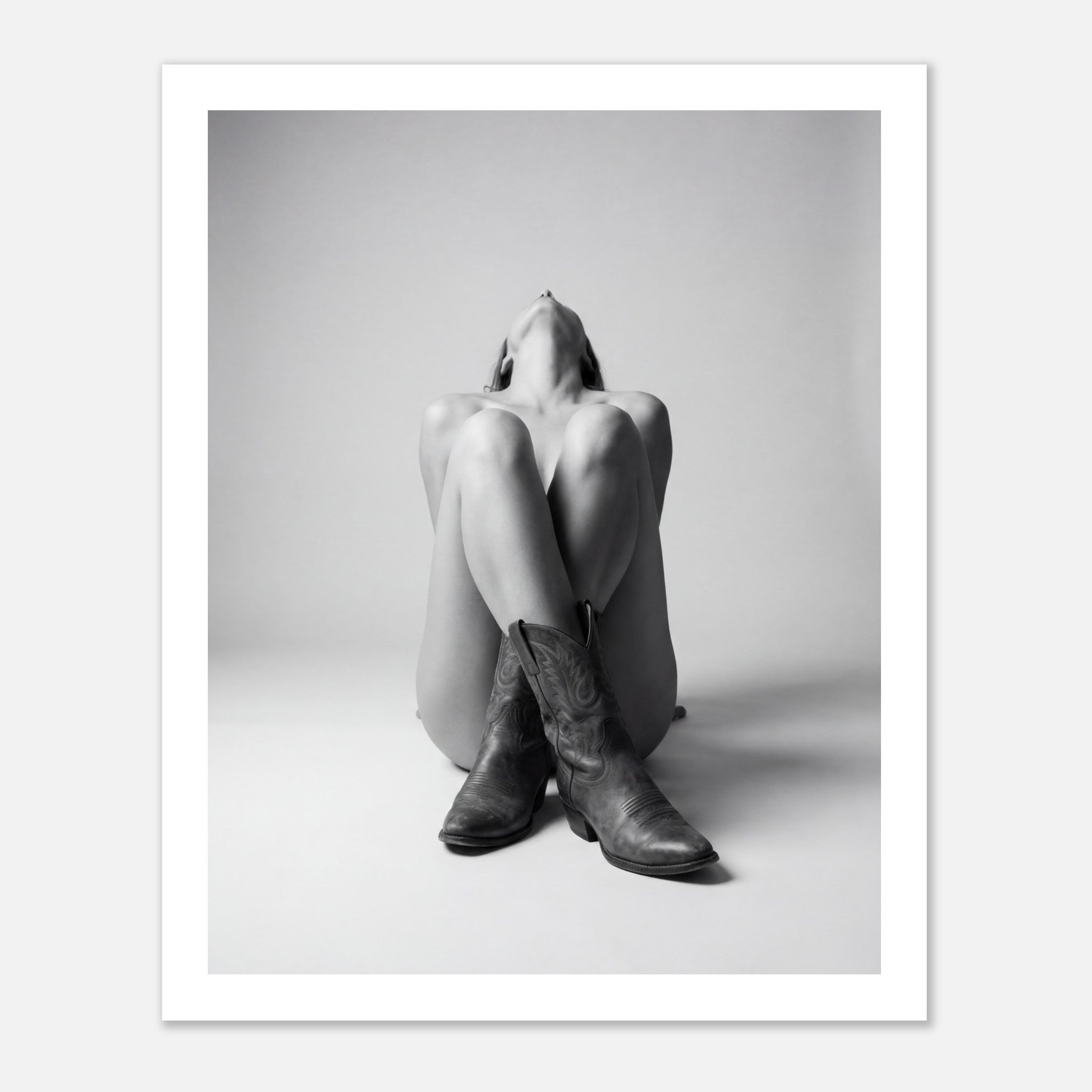 Black and white fine art poster of a seated cowgirl figure wearing classic cowboy boots against a minimalist studio background, creating a dramatic western-inspired composition.