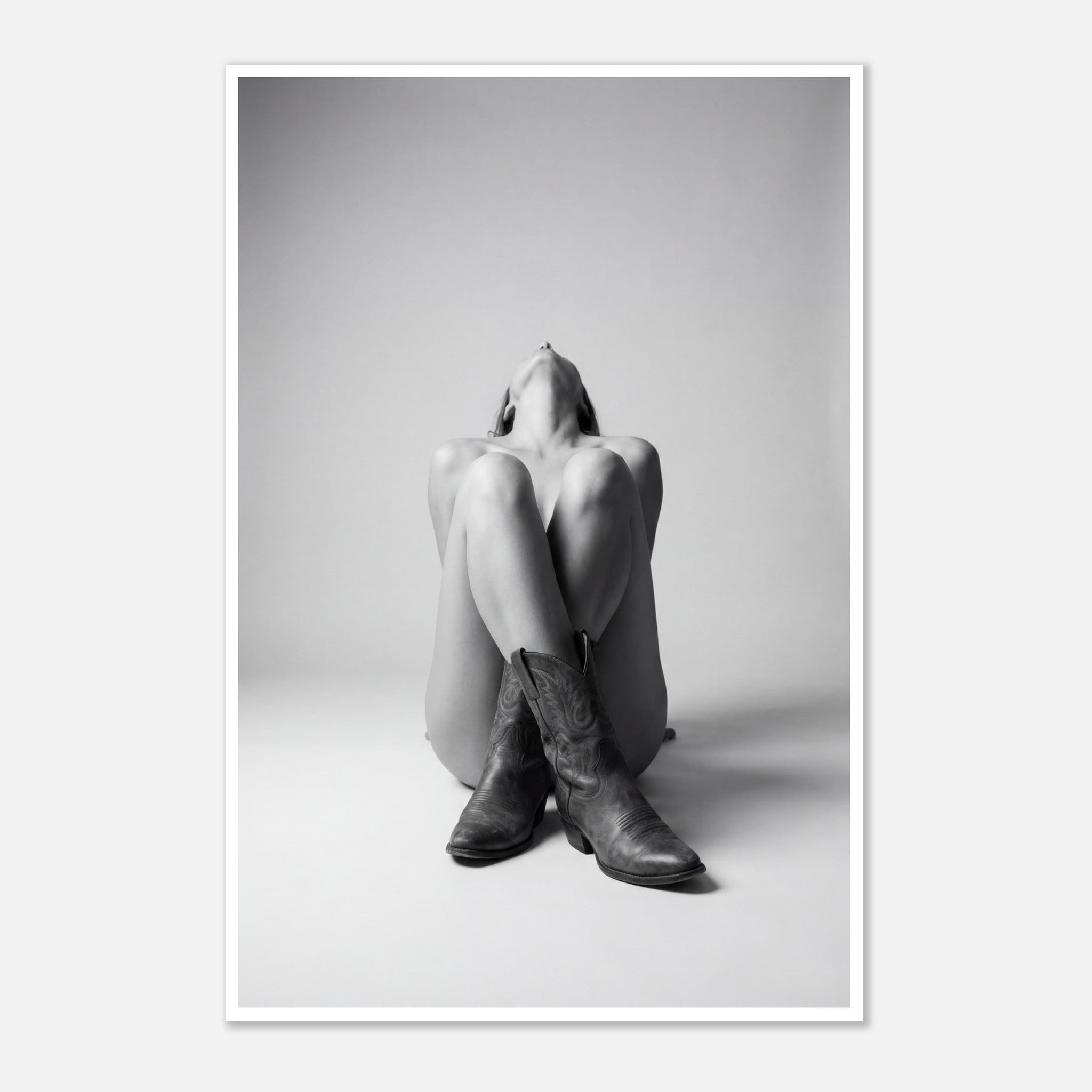 Black and white fine art poster of a seated cowgirl figure wearing classic cowboy boots against a minimalist studio background, creating a dramatic western-inspired composition.