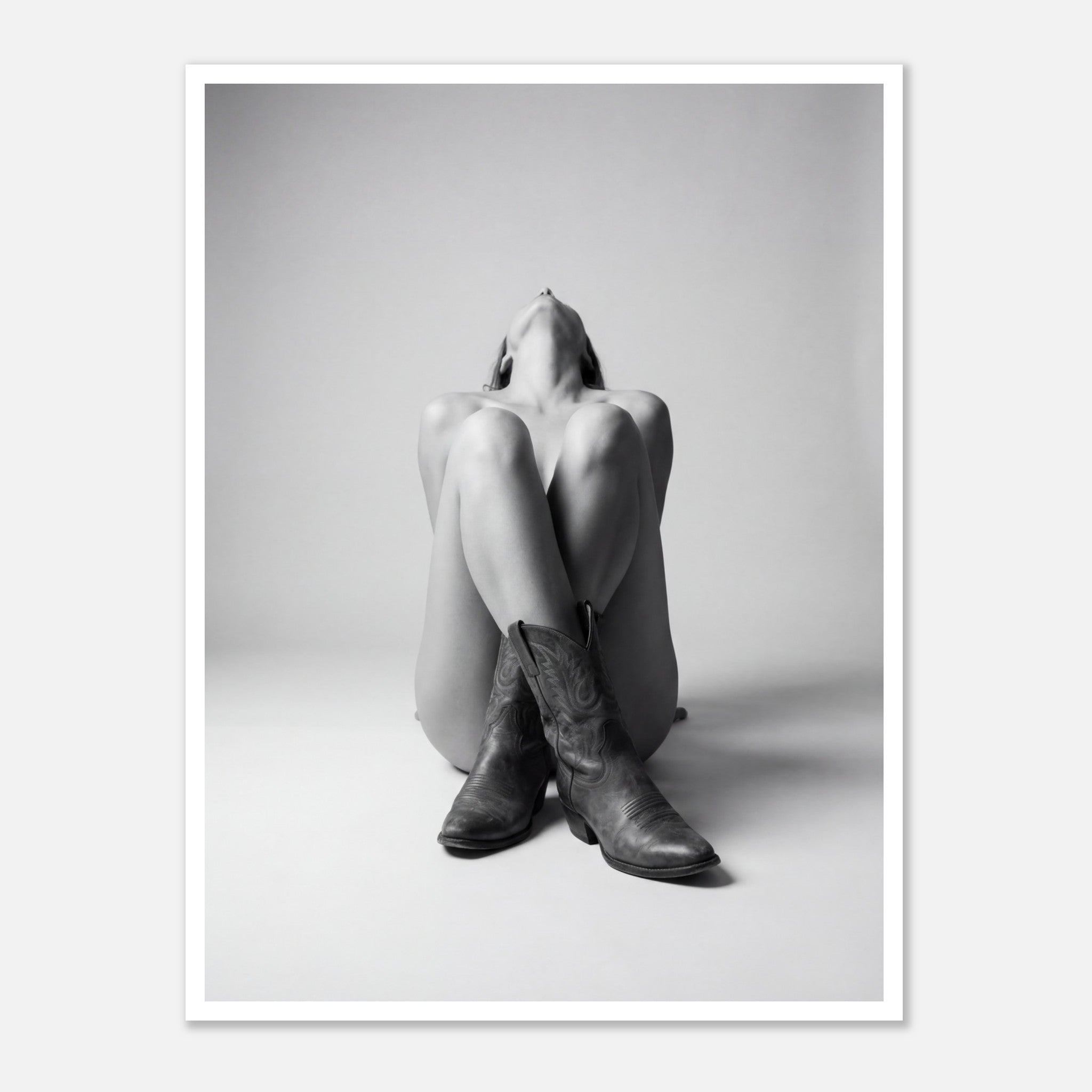 Black and white fine art poster of a seated cowgirl figure wearing classic cowboy boots against a minimalist studio background, creating a dramatic western-inspired composition.
