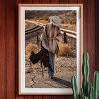 Framed photograph of a cowgirl in a desert landscape with a saddle, against a wooden wall.