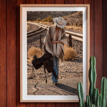 Framed photograph of a cowgirl in a desert landscape with a saddle, against a wooden wall.