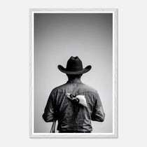 Black and white photograph of a rodeo cowboy viewed from behind wearing a western hat with a numbered rodeo tag pinned to his shirt after competition.