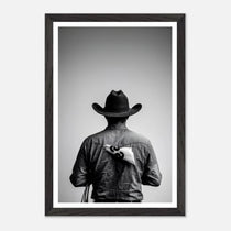 Black and white photograph of a rodeo cowboy viewed from behind wearing a western hat with a numbered rodeo tag pinned to his shirt after competition.