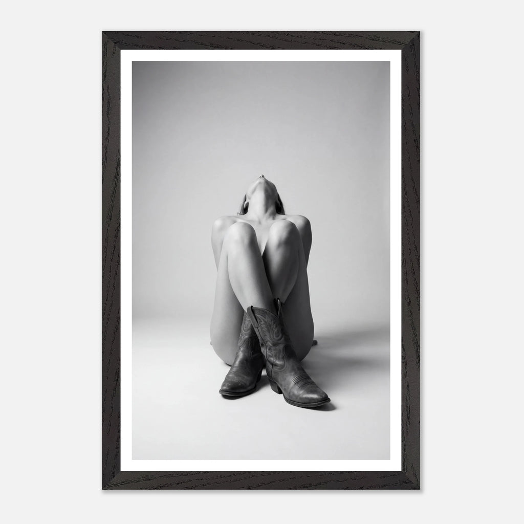 Framed black and white photo of a person sitting with legs crossed wearing cowboy boots.