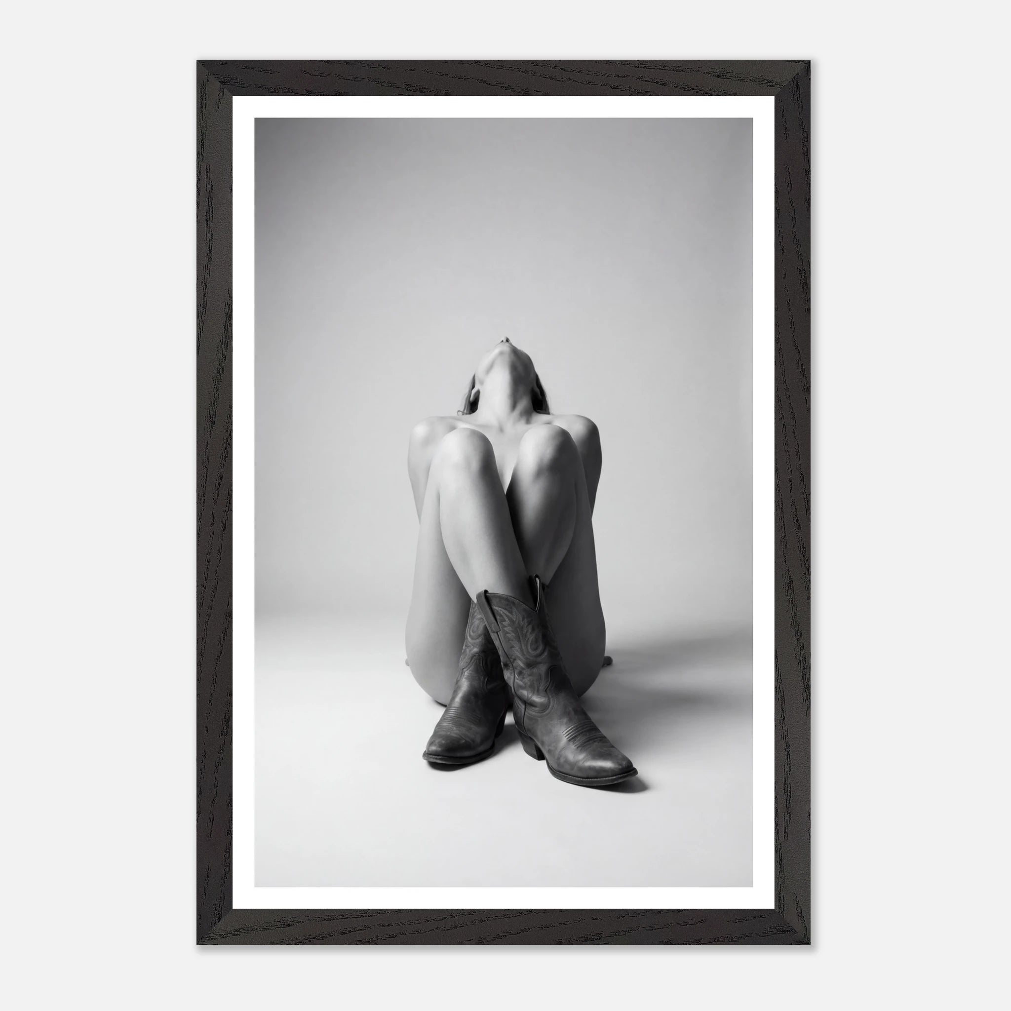 Framed black and white photo of a person sitting with legs crossed wearing cowboy boots.